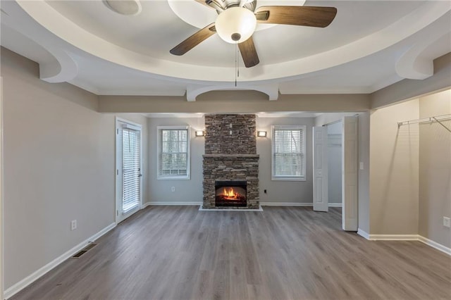 unfurnished living room featuring plenty of natural light, a stone fireplace, a raised ceiling, and light hardwood / wood-style flooring