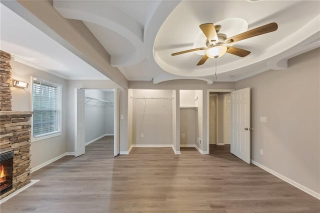 unfurnished bedroom with ceiling fan, a stone fireplace, two closets, and light wood-type flooring