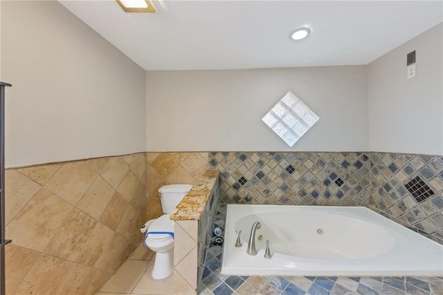 bathroom with tile patterned flooring, a skylight, tiled bath, and toilet