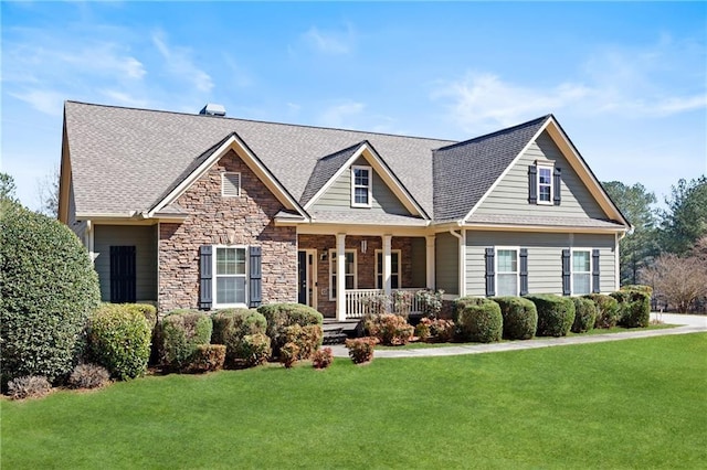 craftsman inspired home with a porch, stone siding, a shingled roof, and a front lawn