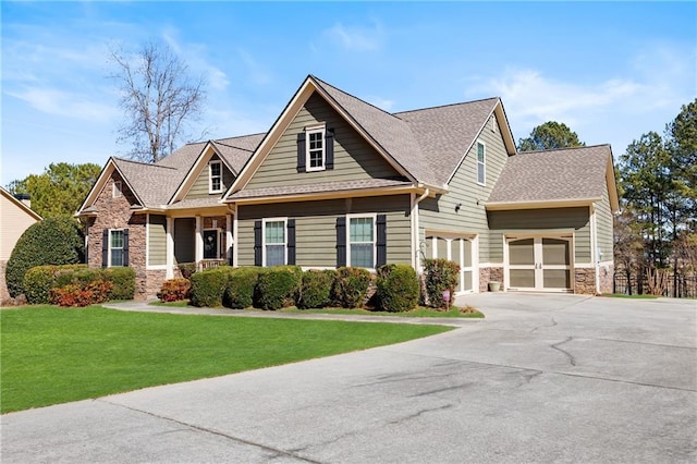 craftsman inspired home featuring driveway, stone siding, a shingled roof, and a front lawn