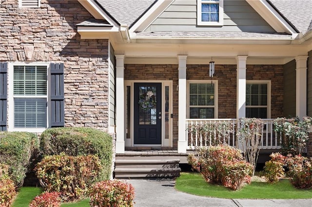 doorway to property featuring a porch, stone siding, and roof with shingles