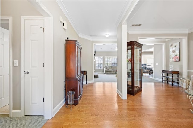 interior space with ornamental molding, light wood finished floors, visible vents, and baseboards