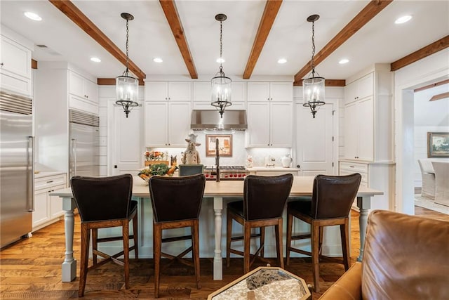 kitchen featuring built in fridge, white cabinetry, hanging light fixtures, and a kitchen island with sink