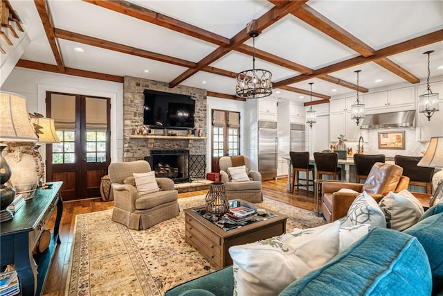 living room featuring french doors, coffered ceiling, a large fireplace, a notable chandelier, and hardwood / wood-style floors