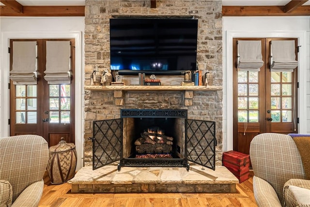 living room featuring french doors, wood-type flooring, a stone fireplace, and beam ceiling