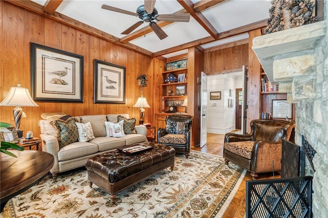 living room featuring a fireplace, wood walls, ceiling fan, beam ceiling, and built in shelves