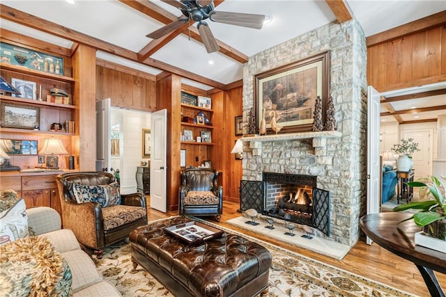 living room with built in features, beam ceiling, a stone fireplace, and light hardwood / wood-style floors