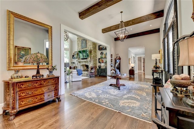 interior space with hardwood / wood-style flooring, beamed ceiling, a stone fireplace, and an inviting chandelier