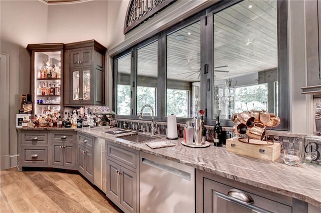 bar featuring light stone countertops, light hardwood / wood-style floors, sink, ceiling fan, and stainless steel dishwasher