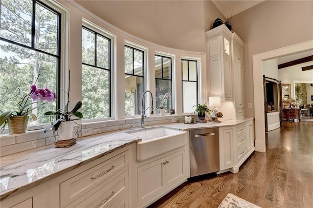 kitchen featuring light stone countertops, a barn door, stainless steel dishwasher, sink, and white cabinets