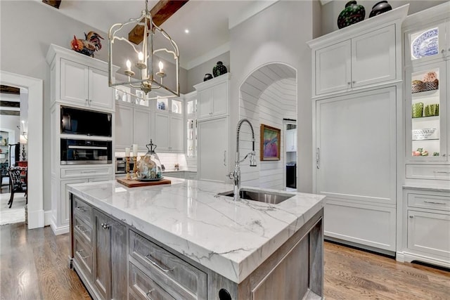 kitchen with decorative light fixtures, white cabinetry, an island with sink, sink, and light stone counters