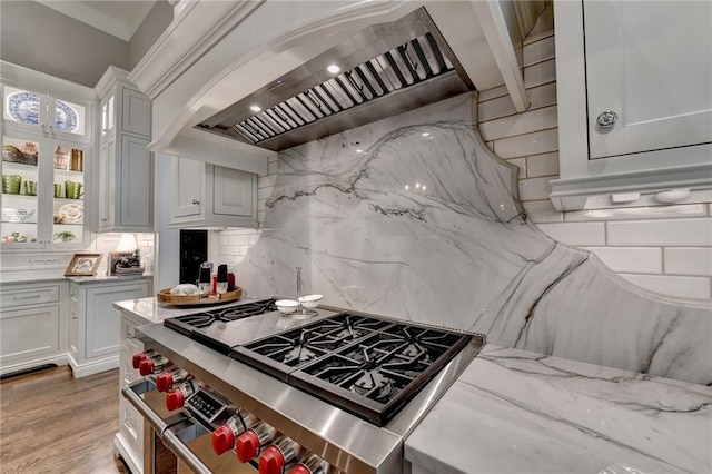 kitchen featuring stainless steel stove, white cabinets, and wall chimney range hood