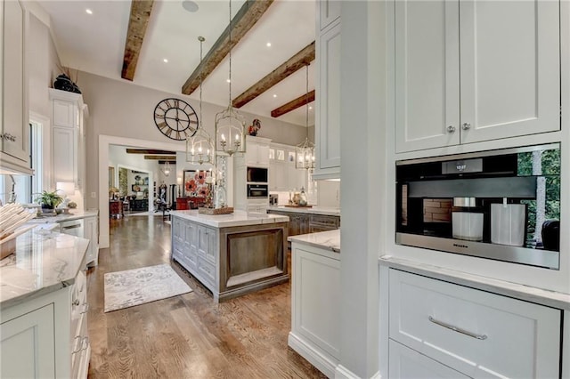 kitchen with light stone countertops, pendant lighting, white cabinets, a kitchen island, and beam ceiling