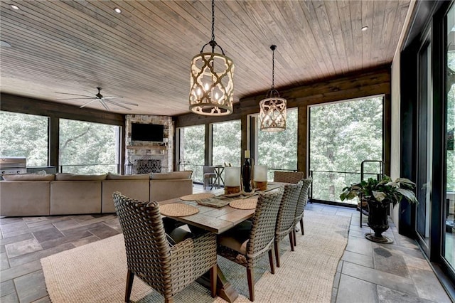 dining area featuring ceiling fan, a stone fireplace, and wooden ceiling