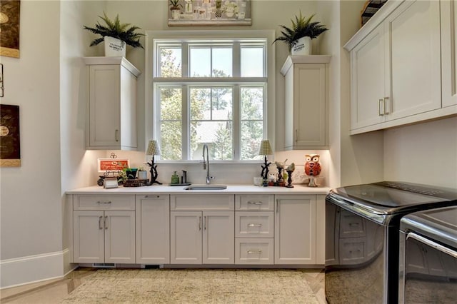 clothes washing area with sink, washer and clothes dryer, and cabinets