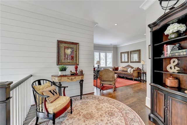 sitting room featuring wood walls, wood-type flooring, and crown molding