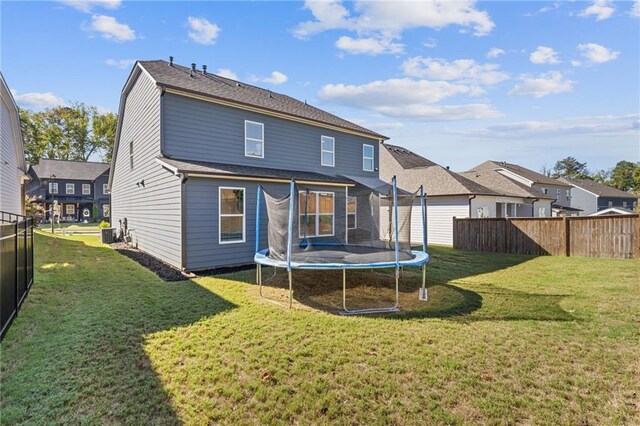 back of property with central AC unit, a trampoline, and a yard