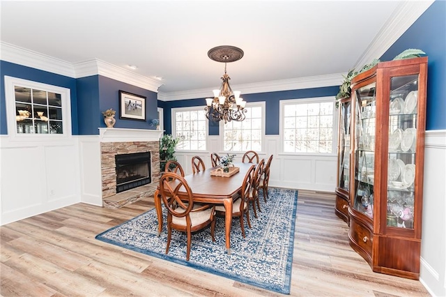 dining room with a chandelier, a stone fireplace, light wood-style flooring, and a wealth of natural light