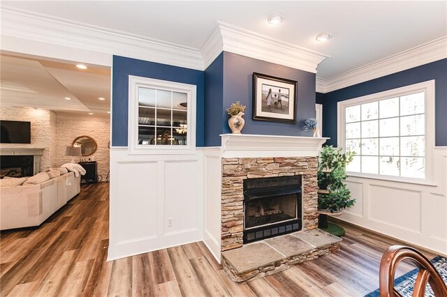 living room with wood finished floors, a wainscoted wall, a fireplace, ornamental molding, and a decorative wall