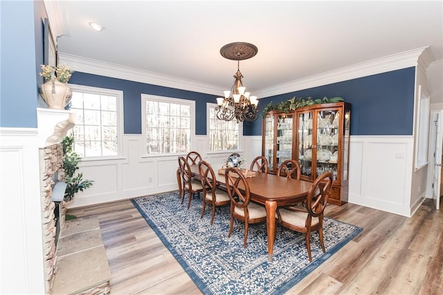 dining room with a wainscoted wall, crown molding, a notable chandelier, and light wood-type flooring