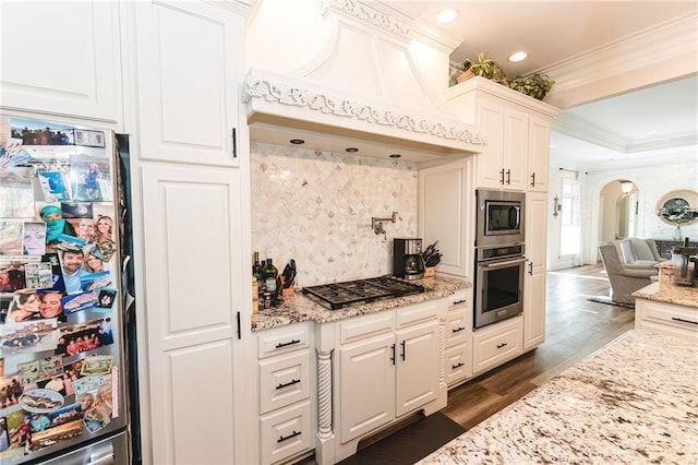 kitchen featuring premium range hood, dark wood-type flooring, ornamental molding, stainless steel appliances, and arched walkways