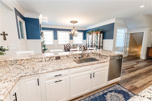 kitchen with a wainscoted wall, a notable chandelier, a sink, stainless steel dishwasher, and crown molding