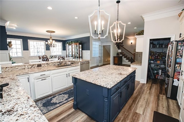 kitchen featuring blue cabinets, a notable chandelier, a sink, appliances with stainless steel finishes, and wainscoting