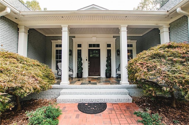 view of exterior entry featuring brick siding and a porch