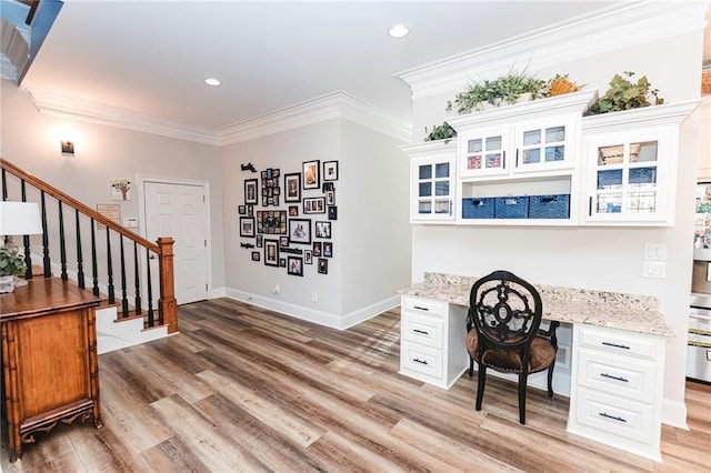 office area featuring light wood-type flooring, baseboards, built in desk, and ornamental molding