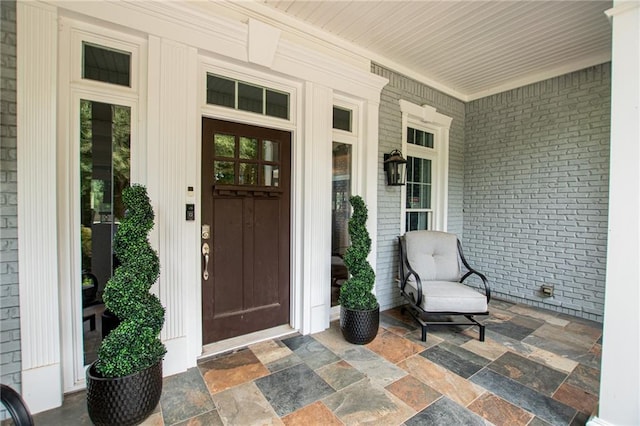 view of exterior entry with brick siding and a porch