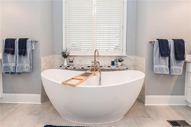 bathroom with a freestanding tub, visible vents, and wainscoting