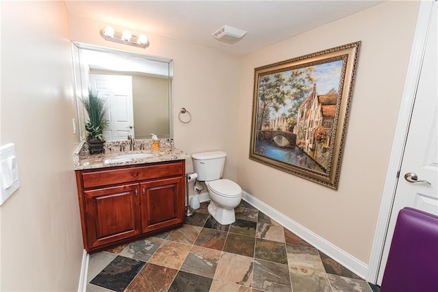 bathroom featuring visible vents, toilet, stone finish floor, baseboards, and vanity