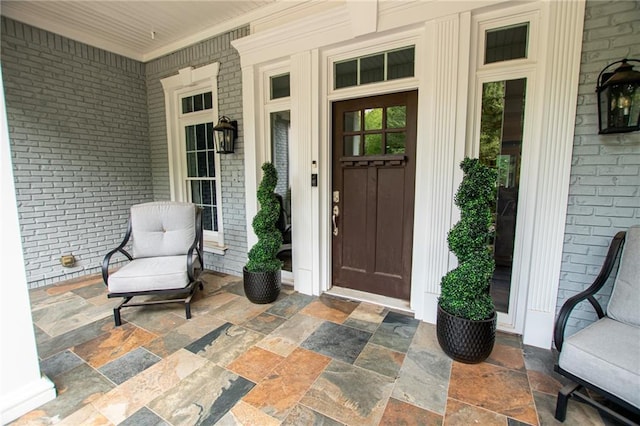 view of exterior entry with brick siding and a porch