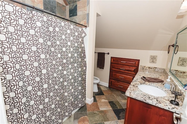 full bath featuring vanity, baseboards, stone tile flooring, vaulted ceiling, and toilet