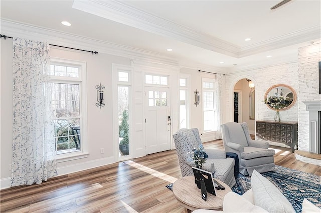 entryway with arched walkways, light wood-style floors, a raised ceiling, and crown molding