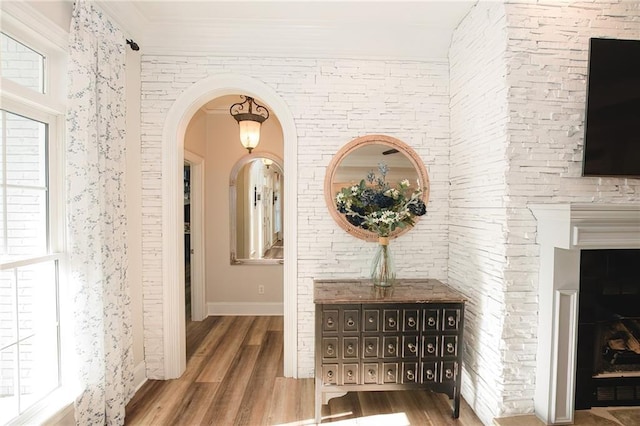 hallway with arched walkways, ornamental molding, and wood finished floors