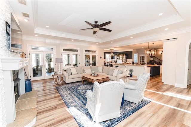 living room featuring light wood finished floors, a fireplace with flush hearth, ceiling fan with notable chandelier, and a raised ceiling