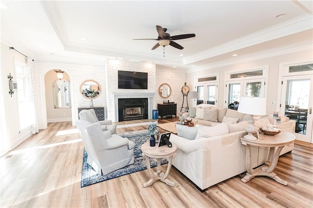 living area featuring arched walkways, light wood finished floors, a ceiling fan, and a tray ceiling