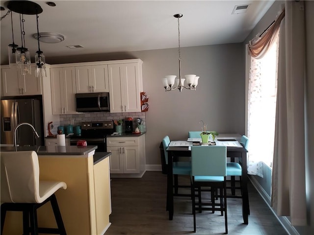 kitchen featuring a breakfast bar area, hanging light fixtures, stainless steel appliances, and white cabinetry