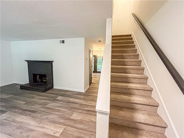 3150 Stratford Green Pl, Avondale Estates, GA 30002 - stairway featuring wood finished floors, a textured ceiling, a brick fireplace, and a chandelier