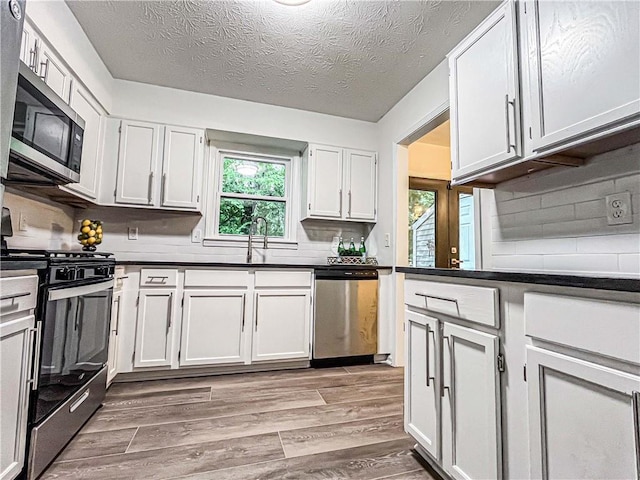 3150 Stratford Green Pl, Avondale Estates, GA 30002 - kitchen featuring appliances with stainless steel finishes, light wood-style floors, dark countertops, backsplash, and a textured ceiling