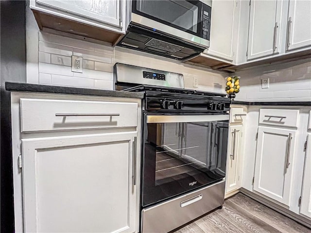 3150 Stratford Green Pl, Avondale Estates, GA 30002 - kitchen featuring appliances with stainless steel finishes, dark countertops, light wood finished floors, decorative backsplash, and white cabinets