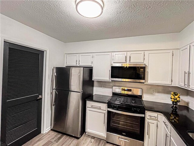 3150 Stratford Green Pl, Avondale Estates, GA 30002 - kitchen featuring appliances with stainless steel finishes, light wood-style floors, white cabinets, dark countertops, and a textured ceiling