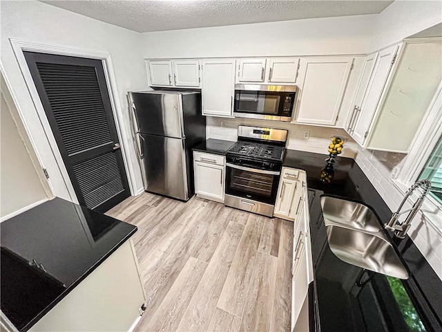 3150 Stratford Green Pl, Avondale Estates, GA 30002 - kitchen with stainless steel appliances, light wood finished floors, dark countertops, a textured ceiling, and white cabinets