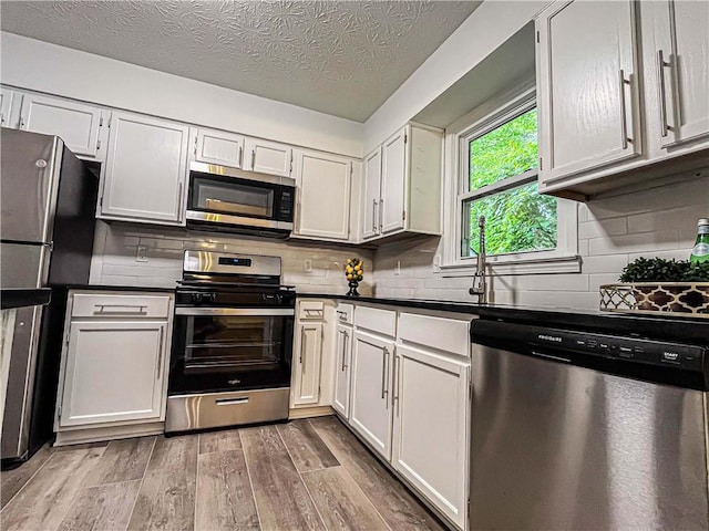 3150 Stratford Green Pl, Avondale Estates, GA 30002 - kitchen with appliances with stainless steel finishes, light wood-style flooring, dark countertops, backsplash, and a textured ceiling