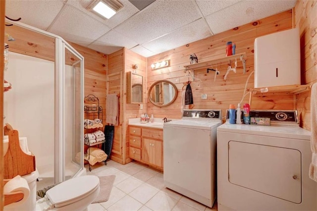 laundry room featuring light tile patterned floors, wooden walls, washer and dryer, and sink