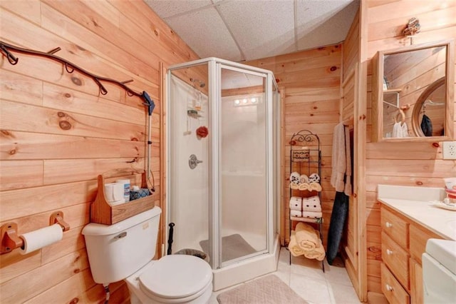 bathroom with toilet, a paneled ceiling, wooden walls, a shower with door, and vanity