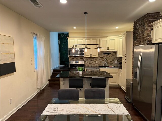 kitchen with a kitchen bar, decorative light fixtures, a center island, stainless steel appliances, and white cabinets