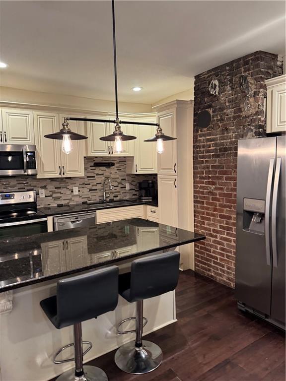 kitchen with sink, dark stone countertops, appliances with stainless steel finishes, dark hardwood / wood-style floors, and backsplash